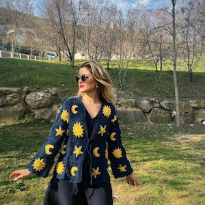 May include: A blue crocheted cardigan with yellow embroidered suns, moons, and stars. The cardigan has a tie closure at the front.