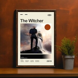 Pu&ograve; includere: Un poster incorniciato di "The Witcher" con un'immagine centrale di due figure su una cima rocciosa. Il poster ha un design minimalista con il titolo in grassetto, un cerchio marrone e l'anno 2019.