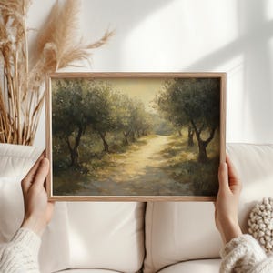 Puede incluir: Pintura enmarcada de un paisaje que representa un camino soleado a trav&eacute;s de un olivar. La obra presenta olivos que bordean el camino, con una paleta de colores suaves y c&aacute;lidos de verdes, marrones y amarillos. El marco es de madera clara.