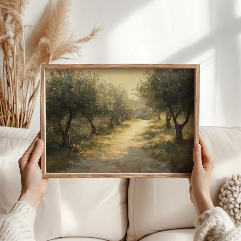 Puede incluir: Pintura enmarcada de un paisaje que representa un camino soleado a trav&eacute;s de un olivar. La obra presenta olivos que bordean el camino, con una paleta de colores suaves y c&aacute;lidos de verdes, marrones y amarillos. El marco es de madera clara.