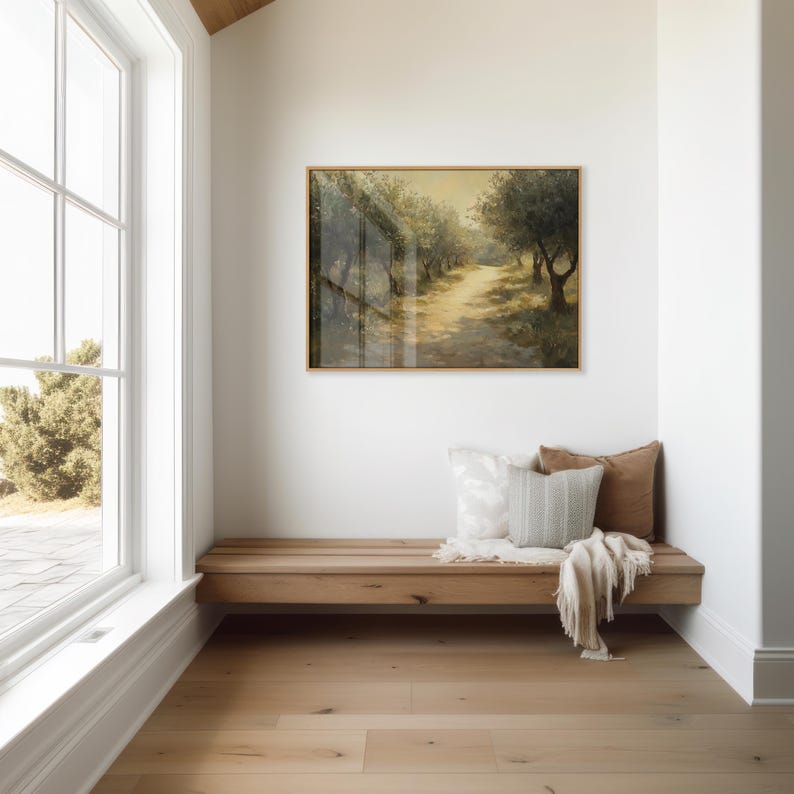 Puede incluir: Una pintura de paisaje enmarcada de un camino bordeado de olivos cuelga sobre un banco de madera. El banco tiene cojines decorativos y una manta doblada. La habitaci&oacute;n tiene una ventana grande y suelo de madera clara.