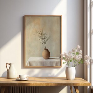 May include: A framed painting of a single brown vase with a leafy branch on a white tablecloth. The painting is hanging on a white wall with a wooden frame.