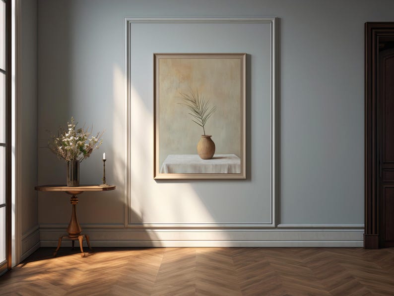 May include: A still life painting of a single branch with leaves in a brown ceramic vase on a white tablecloth. The painting is framed and hanging on a light blue wall.