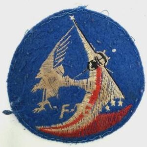 May include: A circular blue embroidered patch featuring a tan bird in flight, a red crescent shape, and the letters F-6 stitched in tan thread. The design includes a star at the top and small star shapes near the bottom right edge of the crescent.