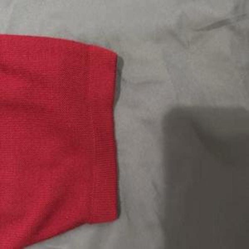 May include: A bright red short sleeve shirt featuring a textured knit fabric. The garment has a distinct ribbed cuff at the end of the sleeve, providing a structured finish to the sleeve edge. The material displays a consistent, fine weave pattern.