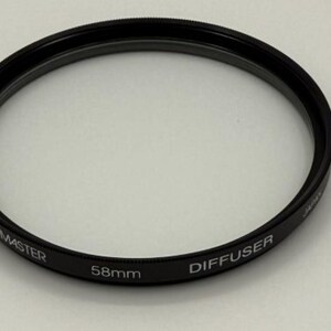 May include: A black ProMaster 58mm diffuser filter for a camera lens. The filter has the word "DIFFUSER" printed on it. The filter is a circular shape.