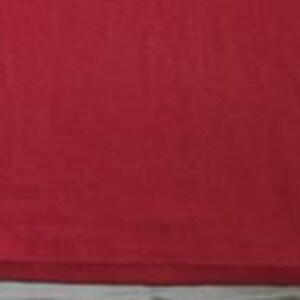 May include: A solid red t-shirt featuring a small white rectangular tag attached to the lower left side seam. The fabric has a visible knit texture and a consistent, vibrant red color throughout the entire garment, ending in a straight hem.