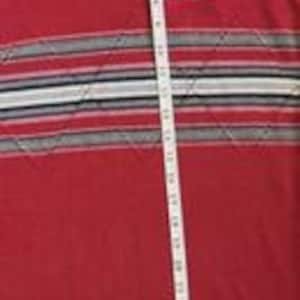 May include: A red long-sleeve shirt featuring a white Artex logo on the chest and a horizontal band with grey, black, and white stripes. A white measuring tape is placed vertically over the shirt, showing a length of approximately 29 inches.