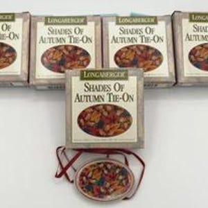 May include: Five Longaberger "Shades of Autumn Tie-On" baskets with matching oval-shaped tie-on ornaments. The baskets are rectangular with a beige and brown color scheme. The tie-on ornaments are oval-shaped with a fall-themed design.