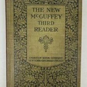 May include: A hardcover book titled The New McGuffey Third Reader with a tan fabric cover. The front features a dark green decorative leaf border, a central leaf emblem, and the text American Book Company New York Cincinnati Chicago.