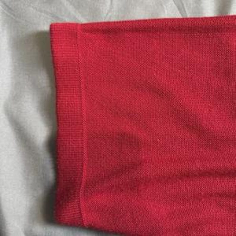 May include: A bright red short-sleeved garment featuring a fine-knit texture and a ribbed cuff detail on the sleeve. The fabric displays a consistent solid red color throughout, with a smooth, uniform weave visible across the entire surface area.