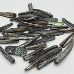 May include: A collection of elongated, dark gray and black shell beads with iridescent, pearlescent surfaces. Each piece features a smooth, tapered shape with a small drilled hole near one end, showcasing natural variations in color and texture.