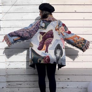 May include: A blue and white tapestry jacket with a fringe trim. The jacket features a pattern of colorful shoes and flowers. The jacket is being worn by a person with black leggings and black boots.