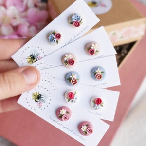 Op de afbeelding: Een set van zes paar handgemaakte polymer clay oorbellen met bloemmotieven. Elk paar wordt getoond op een kaart met de tekst "Designed and crafted with love in Greece".