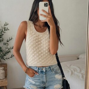 May include: A cream-colored sleeveless crochet top featuring a repeating shell stitch pattern with a round neckline, paired with light blue denim shorts that have a distressed finish, frayed hems, and visible rips on the front panels.
