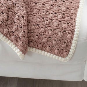 May include: A dusty rose crochet blanket featuring a textured bobble stitch pattern throughout the main body. The blanket is finished with a thick, cream-colored border consisting of a row of small, rounded puff stitches along the entire edge.