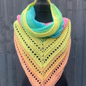 May include: A triangular crochet shawl featuring a vibrant gradient of pastel colours including peach, yellow, lime green, turquoise, and pink. The accessory has an openwork stitch pattern with a pointed bottom edge and is draped around a neck form.