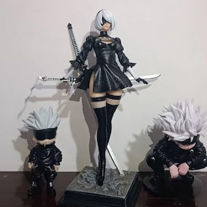 Könnte beinhalten: Drei Actionfiguren, zwei mit weißen Haaren und schwarzer Kleidung und eine mit weißen Haaren und einem schwarzen Kleid. Die Figur im Kleid hält zwei Schwerter.