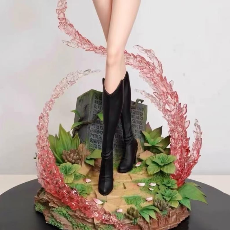 May include: A black and white figure with long legs wearing black boots. The figure is standing on a base with pink and white swirls and green plants.