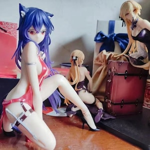 May include: Three anime figurines, two female and one male, posed in a dynamic action scene. The female figurines are wearing colorful outfits and have long, flowing hair. The male figurine is wearing a black suit and has a sword in his hand. The figurines are standing on a wooden surface.
