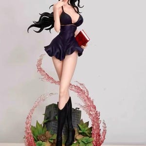 May include: A black and purple anime figurine of a woman with long black hair, wearing a black dress, sunglasses, and black boots. She is holding a red book and standing on a base with green plants and pink and white swirls.