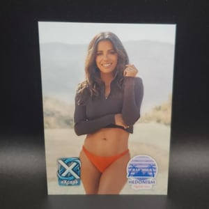 Puede incluir: Fotografía de una mujer con un top de manga larga gris oscuro y una braguita de bikini naranja. La imagen tiene dos logotipos, uno que dice "eXcess" y otro que dice "HEDONISM". El fondo es una escena borrosa al aire libre.