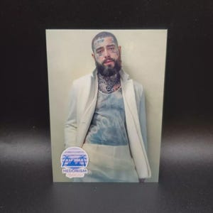 Könnte beinhalten: Rechteckiges Foto eines Mannes mit Gesichtstätowierungen, Bart und weißer Jacke. Das Foto hat unten einen kleinen, kreisförmigen Aufkleber mit dem Wort "HEDONISM" und einem tropischen Design.