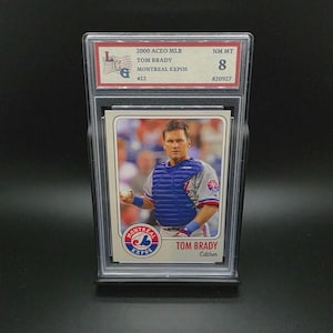 Könnte beinhalten: Eine Baseballkarte mit Tom Brady im Montreal Expos-Trikot. Die Karte befindet sich in einer Schutzhülle und zeigt den Text "2000 ACEO MLB", "TOM BRADY" und "MONTREAL EXPOS". Die Karte ist mit NM MT 8 bewertet.