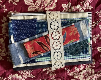 Könnte beinhalten: Eine Sammlung von Stoffresten in verschiedenen Mustern und Farben, darunter Blau, Rot und Grün. Ein cremefarbenes Spitzenband liegt über den Stoffen. Die Stoffe sind auf einer bordeauxfarbenen, floral gemusterten Oberfläche angeordnet.