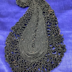 May include: A black paisley-shaped fabric applique with a detailed, intricate design. The applique is made of a woven fabric with a raised, textured surface.