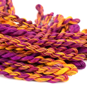 May include: A close-up of a pile of embroidery floss in shades of purple and orange. The floss is twisted together in a braided pattern.