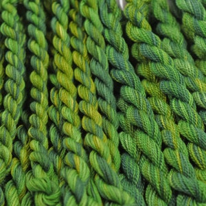 May include: A collection of green and yellow embroidery floss spools. The floss is arranged in rows, with each row featuring a different shade of green.