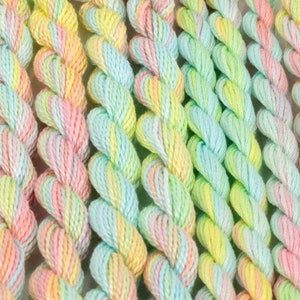May include: A close-up of multiple skeins of embroidery floss in a pastel rainbow color scheme. The floss is twisted and arranged in rows, showcasing the vibrant shades of pink, yellow, and green.