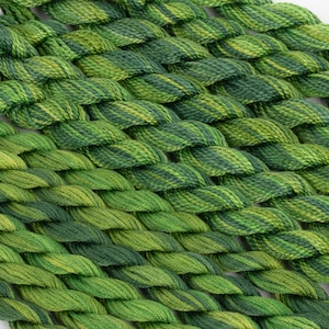 May include: A collection of green and yellow embroidery floss spools, arranged in a braided pattern.