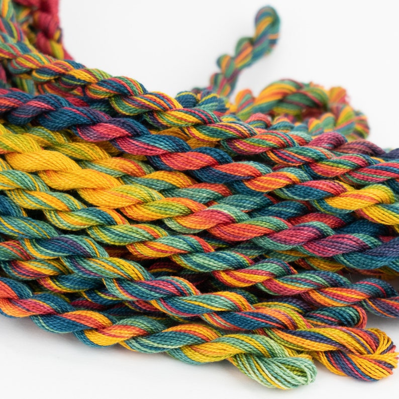 May include: A collection of multi-colored embroidery floss spools in shades of red, orange, yellow, green, blue, and purple. The floss is twisted and piled together in a random pattern.
