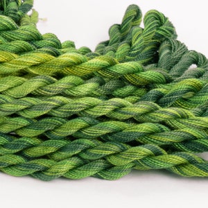 May include: A close-up of a pile of green and yellow embroidery floss. The floss is twisted together in a braid-like pattern.