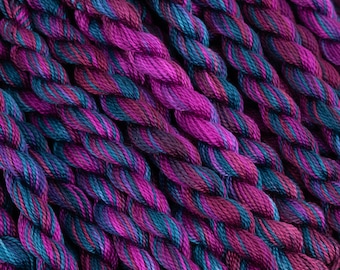 Könnte beinhalten: Nahaufnahme eines Bündels Stickgarn in Violett- und Blautönen. Das Garn ist miteinander verdreht und erzeugt ein strukturiertes und farbenfrohes Muster.