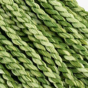 May include: Close-up of a bundle of green and white embroidery floss. The floss is twisted and has a variegated colour pattern.