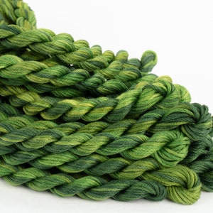 May include: A close-up of a pile of green and yellow embroidery floss. The floss is twisted together in a braid-like pattern.