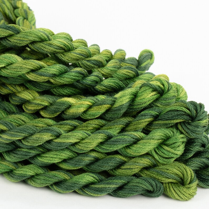 May include: A close-up of a pile of green and yellow embroidery floss. The floss is twisted together in a braid-like pattern.