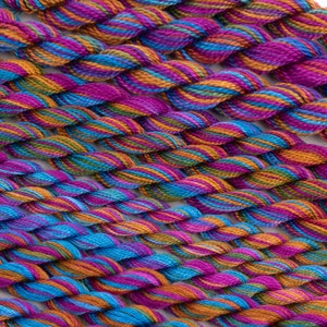 May include: Close-up of a collection of colorful embroidery floss spools. The floss is a mix of orange, blue, green, and purple.