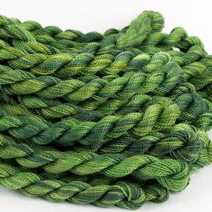 May include: A close-up of a pile of green and yellow embroidery floss. The floss is twisted and piled in a random pattern.