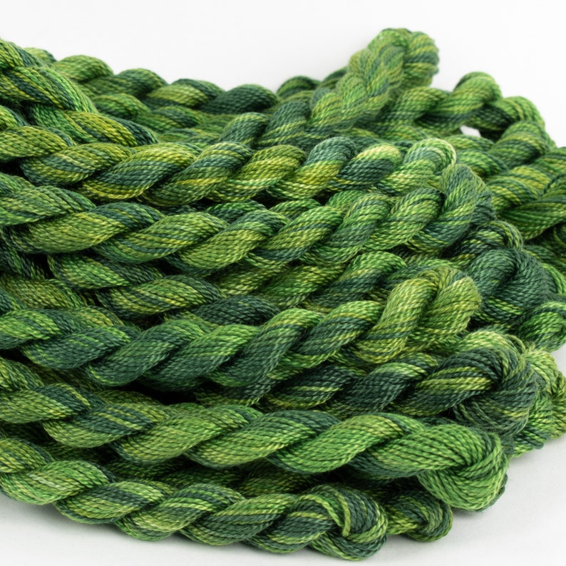 May include: A close-up of a pile of green and yellow embroidery floss. The floss is twisted and piled in a random pattern.