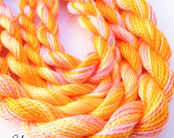 Könnte beinhalten: Nahaufnahme eines Bündels Stickgarn in Orange- und Rosatönen. Das Garn ist miteinander verdreht und erzeugt so eine strukturierte Optik. Das Garn ist mit "Colour Complements" und "COLOURCOMPLEMENTS.COM" beschriftet.