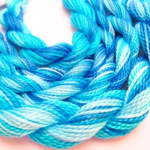 May include: A close-up of a bundle of blue and white embroidery floss. The floss is twisted together in a braid-like pattern.