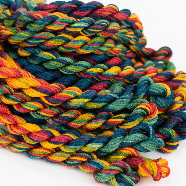 May include: A pile of colorful embroidery floss in shades of red, orange, yellow, green, and blue. The floss is arranged in a loose, tangled pile.