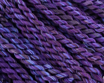 May include: A close-up of a bundle of purple and blue embroidery floss. The floss is twisted and has a variegated color pattern.