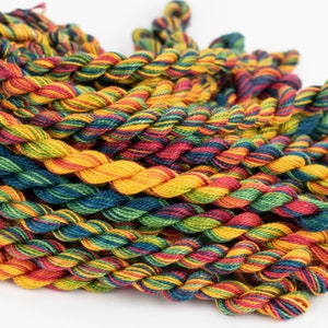 May include: A close-up of a pile of colorful embroidery floss. The floss is twisted and has a variety of colors, including red, yellow, green, and blue.