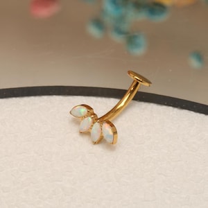 Puede incluir: Joyería corporal de oro con una barra curva y cinco piedras de ópalo blanco en forma de hoja.