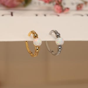 May include: Two small hoop earrings with a white opal stone and beaded accents. One hoop is gold and the other is silver.